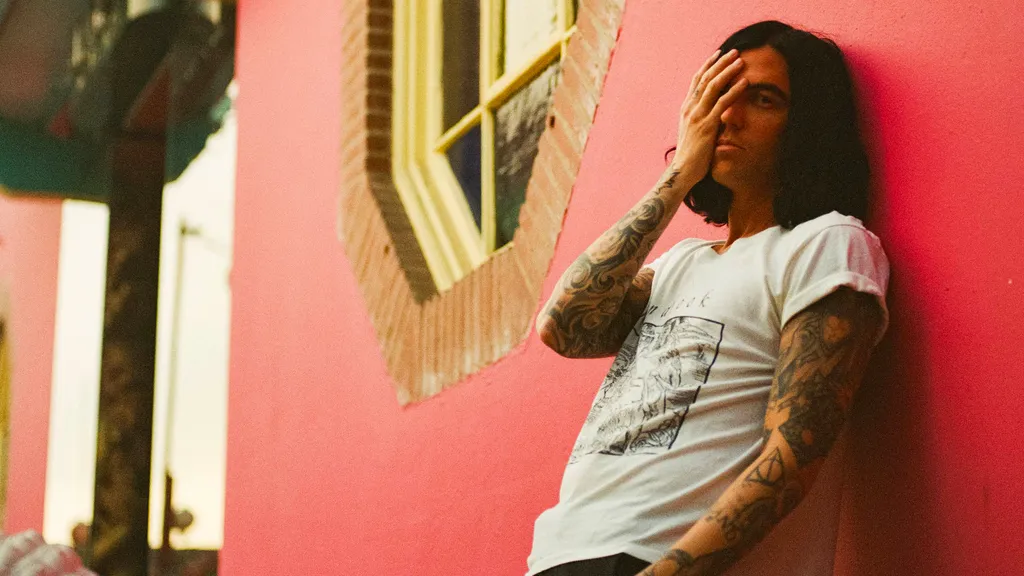 Kellin Quinn leaning against a red wall, photographed by Pooneh Ghana